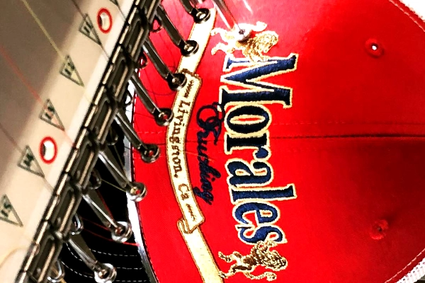 Embroidery machine stitching a Morales Trucking logo on a red cap