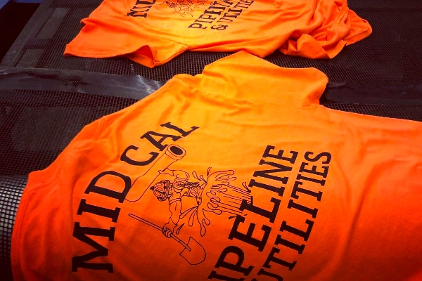 Stack of orange Mid Cal Pipeline & Utilities screen-printed safety tees