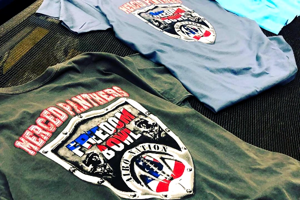 Stack of Merced Panthers Freedom Bowl screen-printed tees in olive and light blue